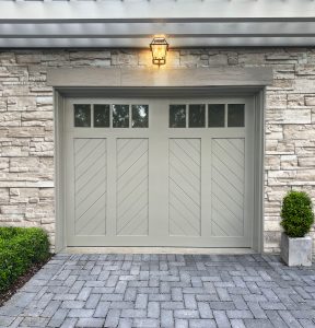 Clopay Canyon Ridge faux wood carriage house garage door with chevron design on a stone home